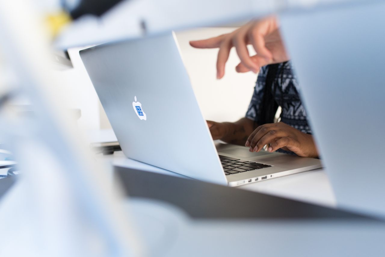 Hands working on a laptop in a modern tech office, showcasing teamwork and technology.