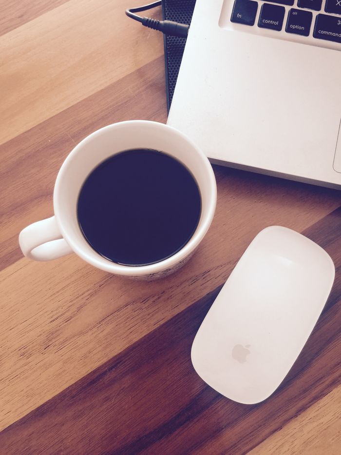 A cup of black coffee next to a laptop and mouse on a wooden desk, perfect for home office vibes.